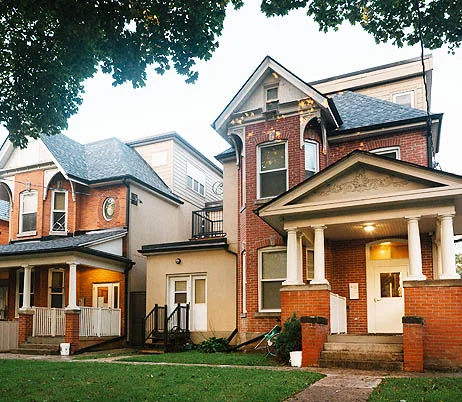 Red brick Victorian house with a white columned porch and gabled roof, home to O'Gitchidaa Mushkiki Wigwam in Parkdale