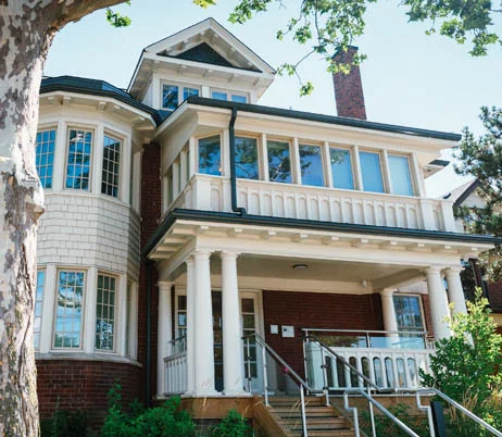 Large brick and stucco house with a wide columned porch, bay windows and an accessible ramp, home to M'iigan Bmikwe in Riverside